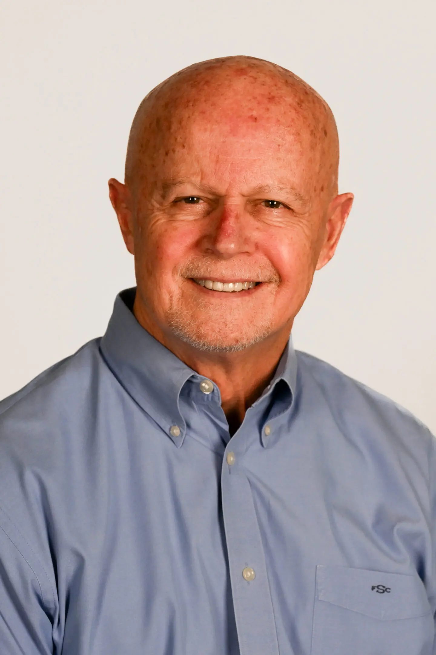 Smiling elderly man in a blue shirt against a plain background.